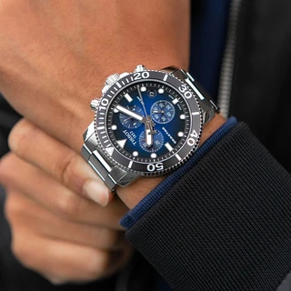 שעון יד לגבר Tissot עם רצועת מתכת, חוגה כחולה עם שלושה מחוגים משניים, נראה בזווית קרובה על פרק היד.